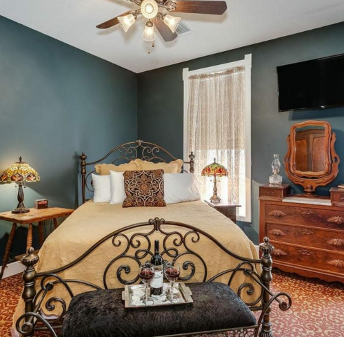 Cozy bedroom with a queen bed, vintage decor, lamps, and a TV, featuring warm colors and a welcoming atmosphere.