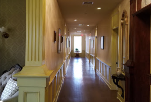 A long, well-lit hallway with yellow walls, framed pictures, and a door at the end leading to natural light.