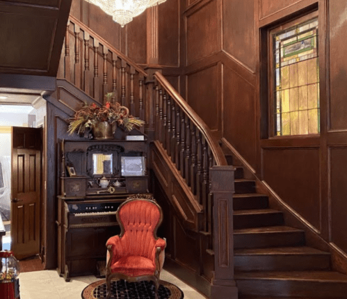 A wooden staircase leads to an upper floor, with a vintage red chair and a decorative stained glass window nearby.