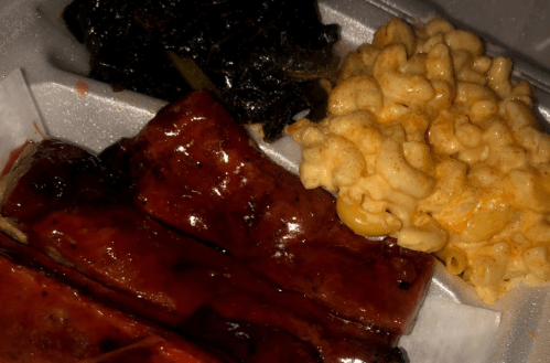 A takeout container with barbecue ribs, collard greens, and macaroni and cheese.