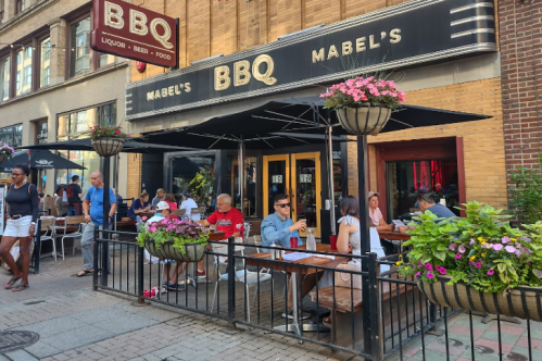 Outdoor dining area of Mabel's BBQ, featuring patrons at tables and vibrant flower planters.