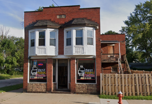 A two-story brick building with bay windows, featuring a sign that reads "Best Thing Around" and an open sign.