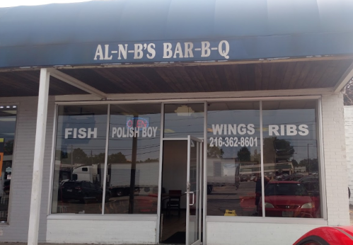 Exterior of Al-N-B's Bar-B-Q featuring a sign and large windows displaying menu items: fish, Polish boy, wings, and ribs.