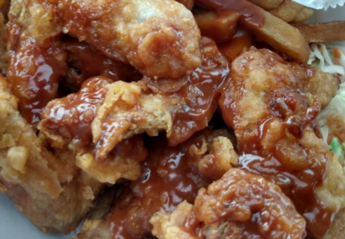 Close-up of crispy fried chicken pieces coated in a rich, tangy sauce, served with fries and coleslaw.