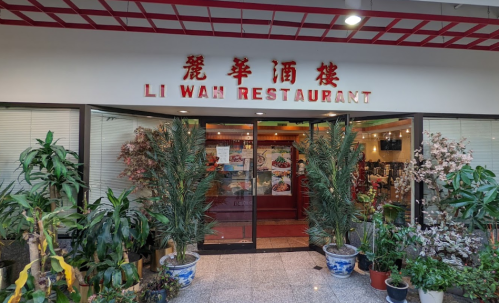 Entrance of Li Wah Restaurant, featuring glass doors, plants, and a sign in red lettering.