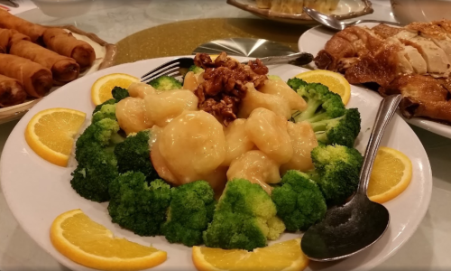 A plate of shrimp in a creamy sauce, served on a bed of broccoli and garnished with orange slices and walnuts.