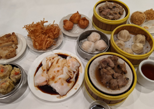 A variety of dim sum dishes including dumplings, buns, and fried items served in bamboo steamers and plates.