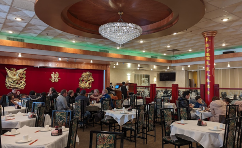 A spacious restaurant interior with elegant decor, featuring round tables, a chandelier, and a red backdrop with gold designs.