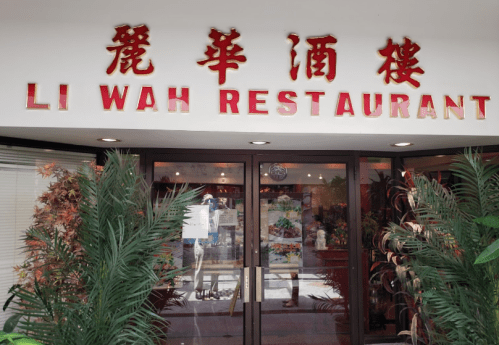 Entrance of Li Wah Restaurant, featuring a sign in red letters and decorative plants on either side.