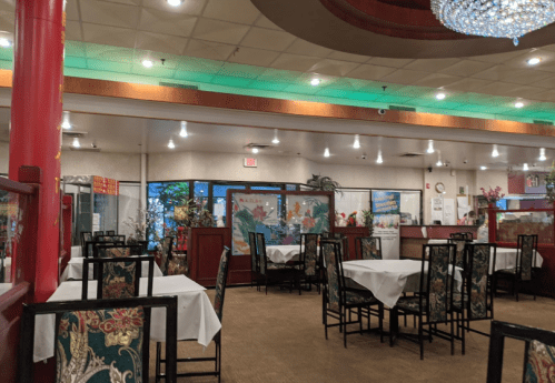 Interior of a restaurant with empty tables, decorative chairs, and plants, featuring a warm, inviting atmosphere.