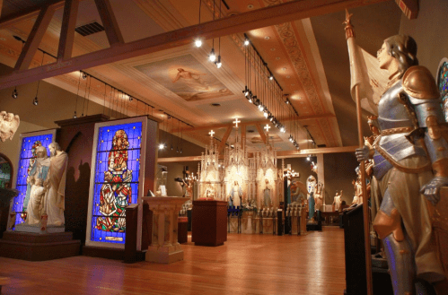 A museum interior featuring stained glass windows, statues, and ornate decor, illuminated by overhead lights.