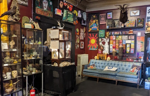 A cozy, eclectic room filled with colorful art, curiosities, and a vintage blue couch against a vibrant wall.