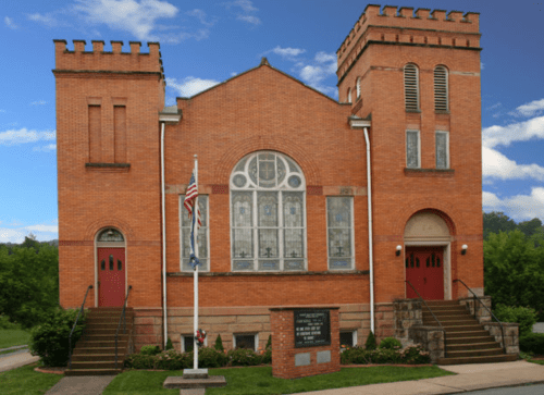 Historic brick church with a decorative facade, two towers, and a flagpole in front, set against a blue sky.