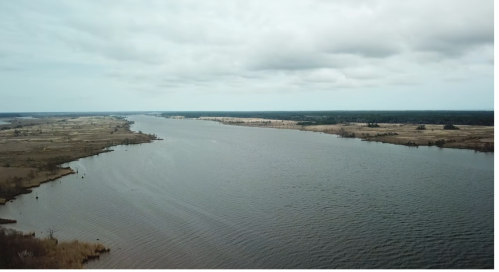 Aerial view of a wide river winding through a landscape of fields and trees under a cloudy sky.