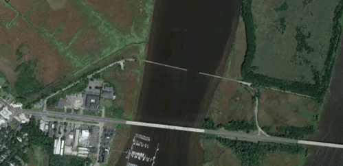 Aerial view of a river with marshland, a highway, and a marina on the left side of the image.