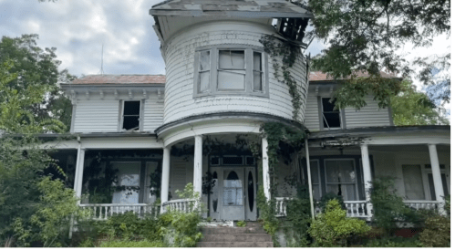 A dilapidated Victorian house with overgrown vines, a circular turret, and broken windows under a cloudy sky.
