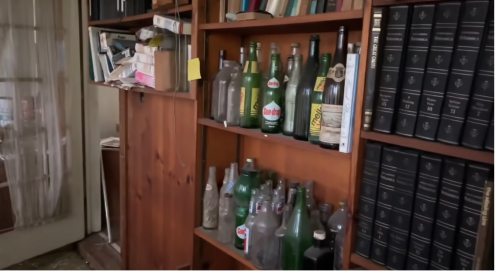A wooden shelf filled with various glass bottles and books, in a dimly lit room.