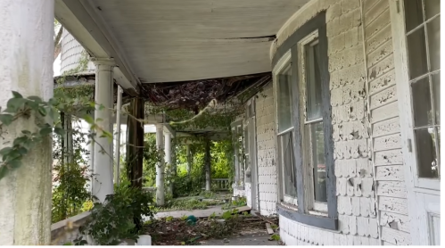An abandoned porch with peeling white paint, overgrown vines, and a partially collapsed roof.
