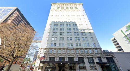 Historic tall building with a white facade, featuring large windows and an entrance, set against a clear blue sky.