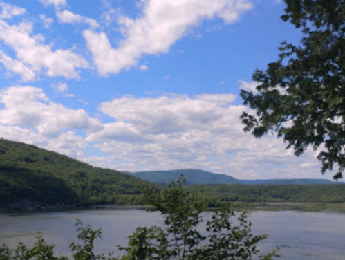 A scenic view of a river surrounded by green hills and a blue sky with fluffy clouds.