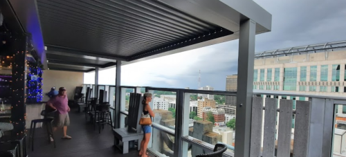 A rooftop terrace with two people overlooking a city skyline under cloudy skies.