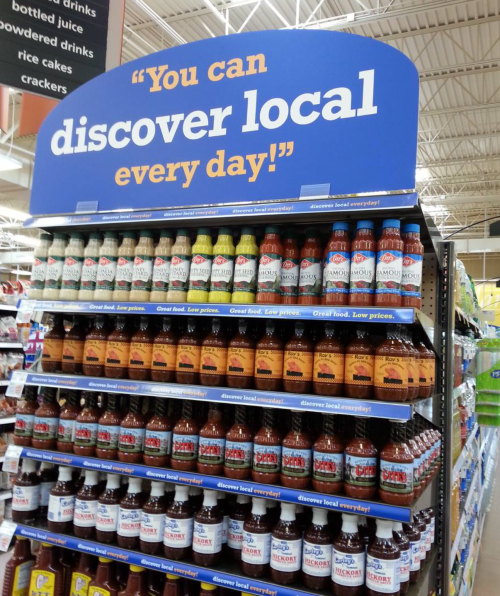 A store display featuring various bottled drinks with a sign that reads, "You can discover local every day!"