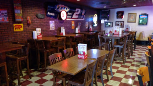 A cozy restaurant interior with wooden tables and chairs, red and white checkered floor, and vintage decor on the walls.