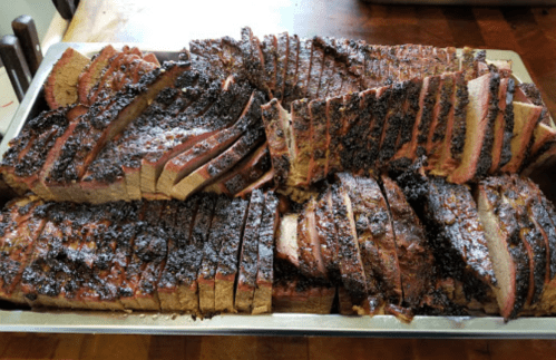 A platter of sliced, smoked brisket with a dark, flavorful crust, arranged neatly in a metal tray.
