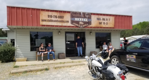 A BBQ restaurant with a red awning, people sitting outside, and a motorcycle parked in front.