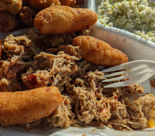 A plate of pulled pork with hushpuppies and coleslaw, served with a plastic fork.