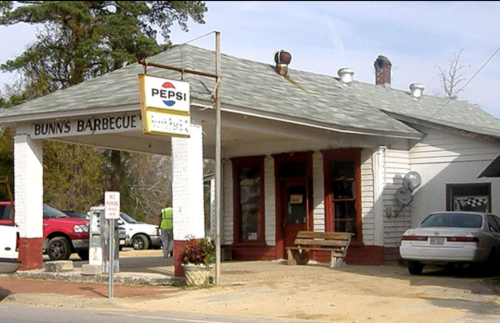 A small barbecue restaurant with a Pepsi sign, featuring a porch and parked cars outside.