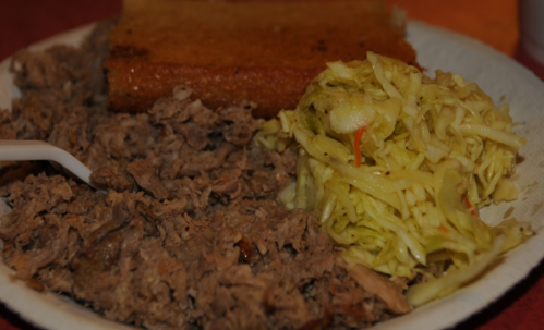 A plate of pulled pork, coleslaw, and cornbread, served with a plastic fork.