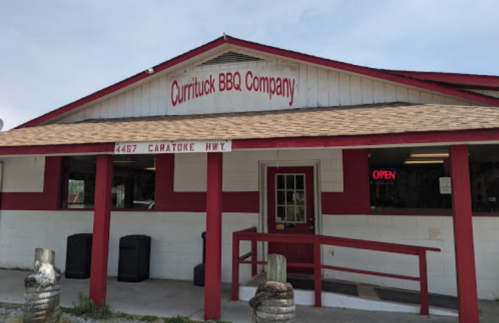 Exterior of Currituck BBQ Company, featuring a red and white building with an "Open" sign and a welcoming entrance.