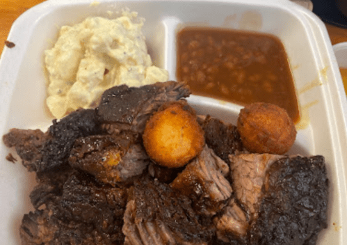 A takeout container with tender beef, cornbread, baked beans, and creamy potato salad.