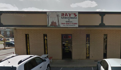 Exterior of Ray's Smokehouse & Grill, featuring a sign and open entrance, with parked cars in front.