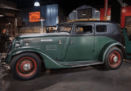 A vintage green and black car with red wheels, displayed in a retro garage setting.
