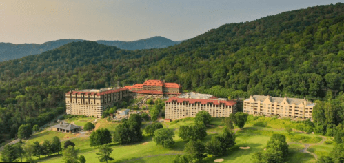Aerial view of a resort nestled in green mountains, featuring multiple buildings and landscaped grounds.