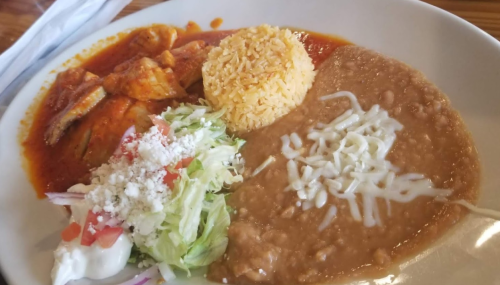 A plate of Mexican food featuring chicken in red sauce, rice, refried beans, and a side salad with cheese and tomatoes.