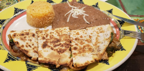 A colorful plate featuring quesadillas, rice, and refried beans topped with cheese.