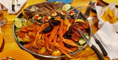 A large seafood platter featuring grilled fish, shrimp, crab, mussels, and garnished with vegetables and lime.