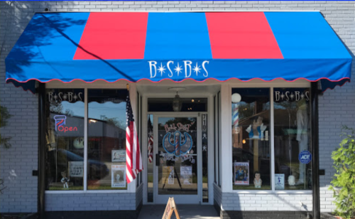 A storefront with a blue and red awning, featuring large windows displaying merchandise and an open sign.