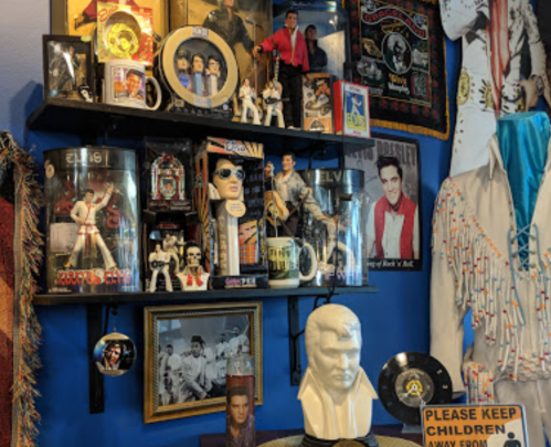 A colorful display of Elvis memorabilia, including photos, figurines, and a bust, on shelves against a blue wall.