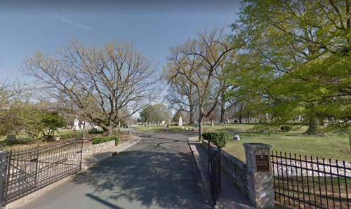 A peaceful cemetery entrance with trees lining the path and a wrought iron gate.