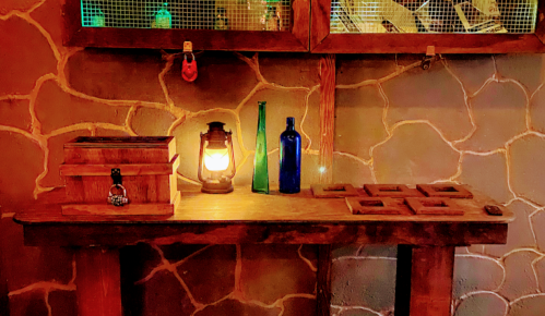 A rustic wooden table with a lantern, blue glass bottle, and a wooden box against a textured wall.