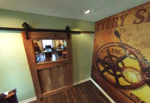 A wooden sliding barn door with a metal track, leading to a room with a decorative gear-themed wall.