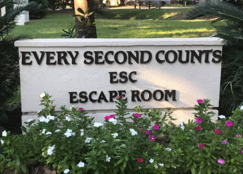 Sign for an escape room reading "Every Second Counts" with colorful flowers in front.