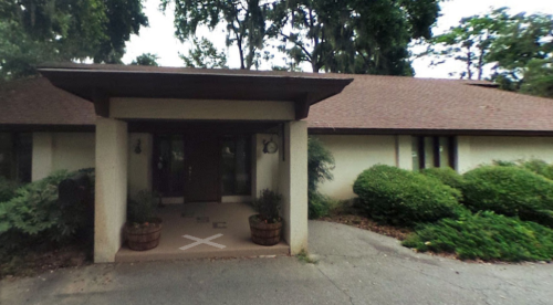 A modern house with a brown roof, front porch, and landscaped bushes in the yard.