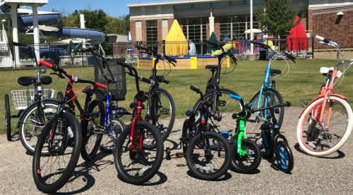 A variety of bicycles in different colors parked on a pavement, with a playground and water slides in the background.