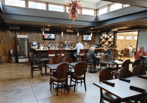 Interior of a restaurant featuring a bar, wooden decor, tables, and patrons dining and socializing.