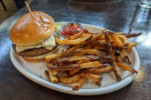 A plate with a burger topped with mayonnaise and a side of crispy fries, accompanied by a small bowl of ketchup.